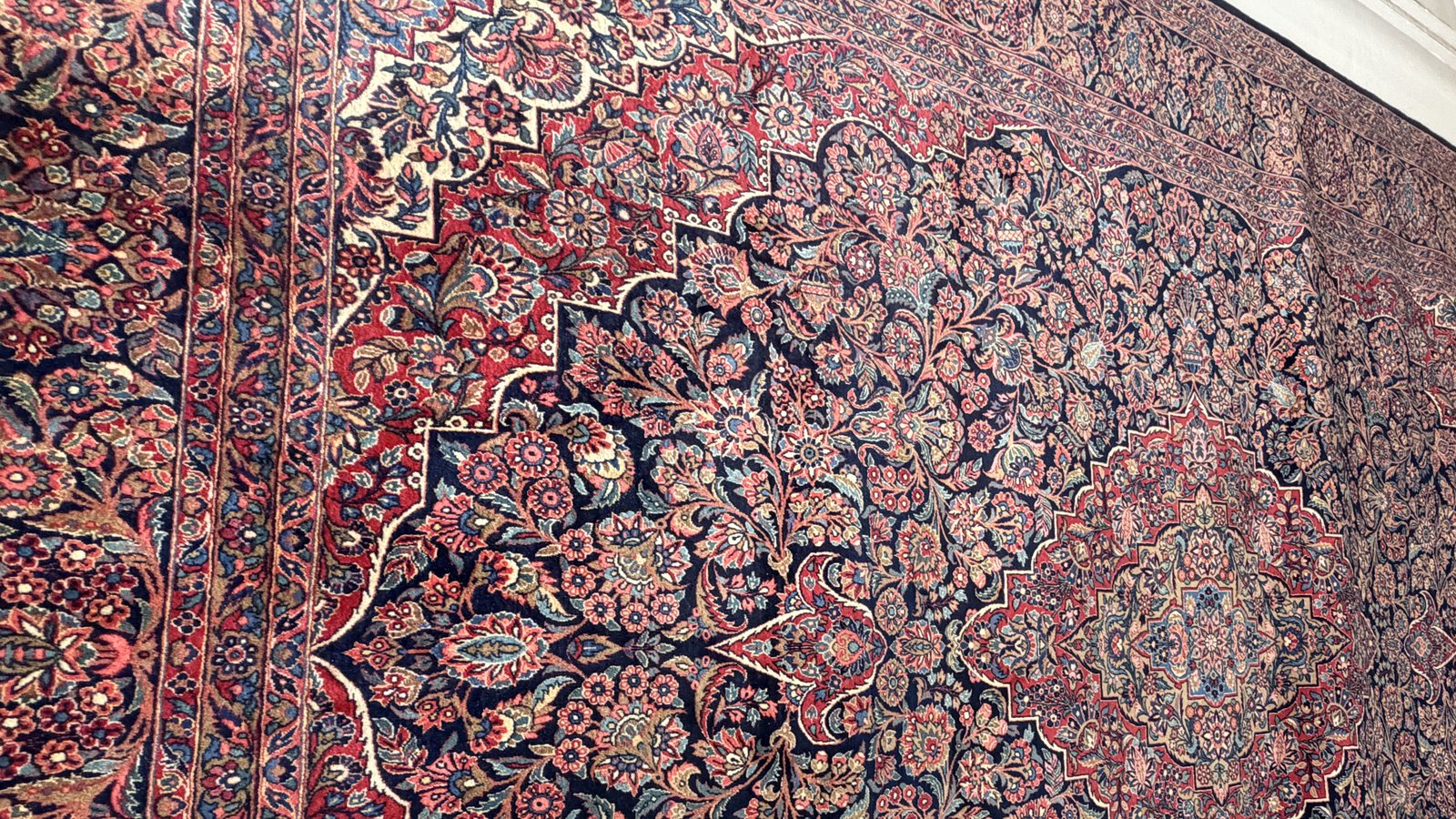 Large antique Persian rug with a floral medallion, hanging for inspection